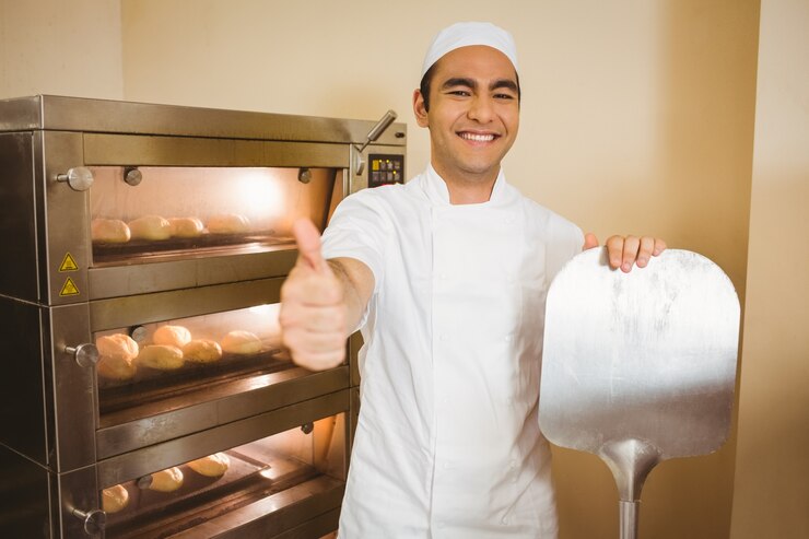Foto baker sonriendo a la cámara al lado del horno