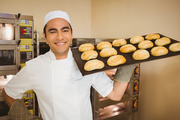Foto baker sonriendo a la cámara sosteniendo la bandeja de rollos