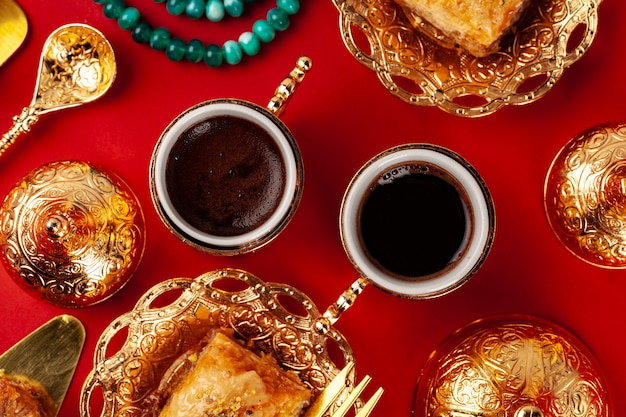 Baklava turco y café en vajilla oriental sobre fondo rojo.