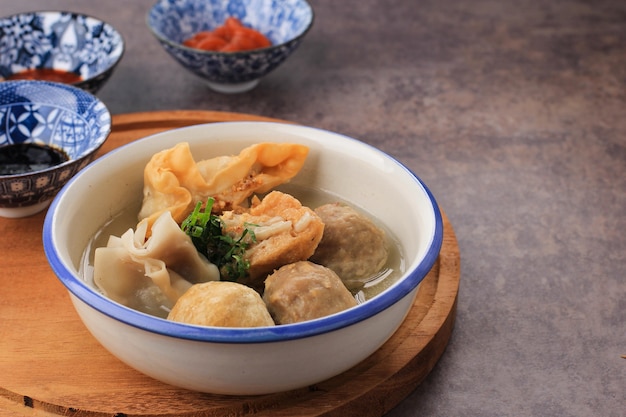 Bakso Arema, especial de comida de albóndigas de Malang, Java Oriental, Indonesia. De cerca, sobre tabla de madera y mesa rústica. Servido con salsa de soja, salsa y pasta de chile