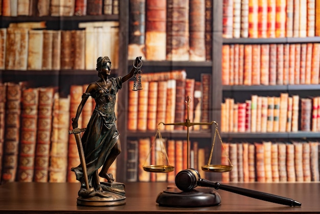 Balanças da estátua da justiça do escritório do advogado e do martelo do juiz contra o pano de fundo de uma parede de livros ou de uma biblioteca Aconselhamento jurídico e conceito de justiça