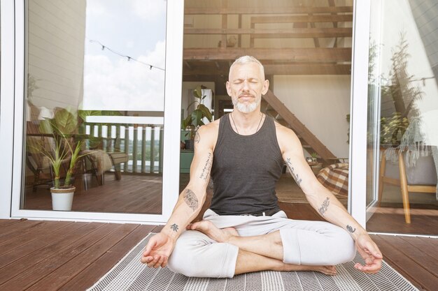 Balance im Leben entspannter kaukasischer Mann mittleren Alters, der in Lotus-Pose auf der sonnigen Terrasse von ihm sitzt