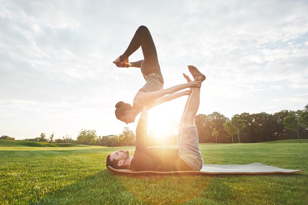 Balancierendes Yoga stellt gesunde und junge Paare dar, die zusammen im Morgenpark Acro-Yoga praktizieren