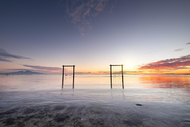 Balanços à beira-mar durante o nascer do sol Céu e reflexos na água no verão Raios de sol durante o nascer do sol Nusa Penida Bali Indonésia Travel image