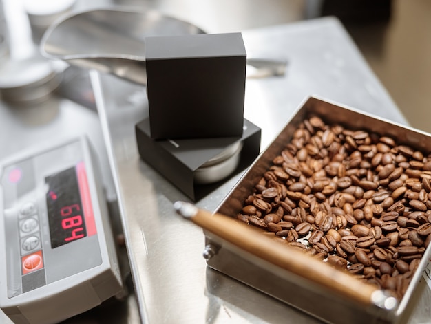 Balanza electrónica con caja negra y granos de café tostados