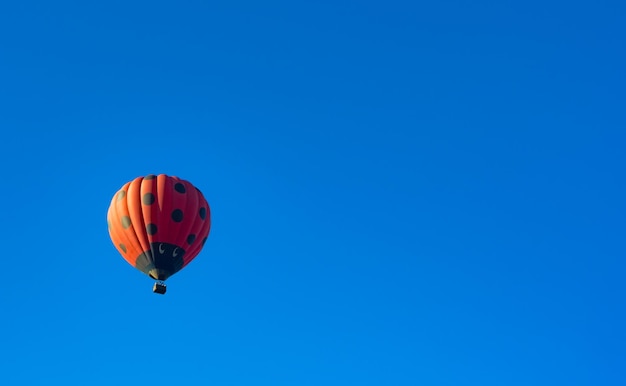 Balão de ar quente vermelho decorado como joaninha voando no céu azul claro