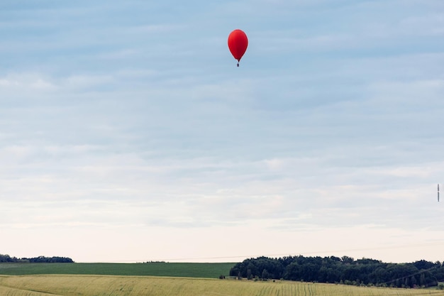 Balão de ar quente vermelho em forma de coração está pousando no campo verde