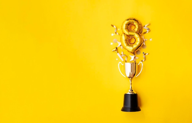 Balão de comemoração de aniversário de ouro número explodindo de um troféu vencedor