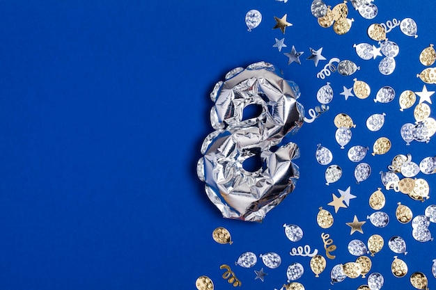 Balão de folha de prata número 8 em um fundo azul com glitter gonfetti
