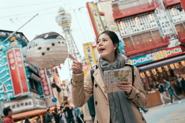 Balão de peixe Fugu pendurado ao ar livre sob o céu azul na área da loja Shinsekai na rua Dotonbori em Osaka Japão. bela dama viajante segurando o mapa de papel e apontar o lado do dedo procurando direção na cidade