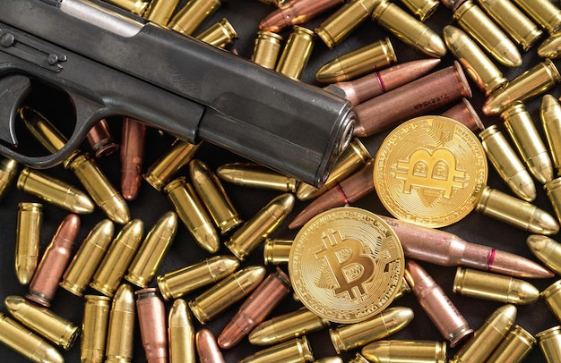 Balas de pistola de bronce y latón esparcidas sobre una mesa oscura, cañón de pistola negra, monedas de bitcoin doradas cerca - uso ilegal de criptomonedas para comprar el concepto de armas