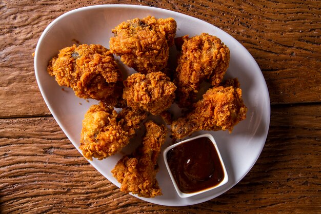 Balde cheio de frango frito kentucky crocante com fumaça e molho de churrasco no fundo marrom. foco seletivo.