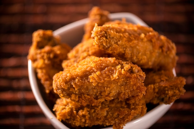 Foto balde cheio de frango frito kentucky crocante com fumaça no fundo marrom. foco seletivo.