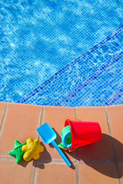 Balde com brinquedos de praia de plástico perto da piscina