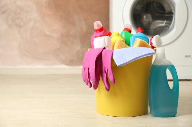 Balde com detergente e produtos de limpeza em fundo marrom, copie o espaço