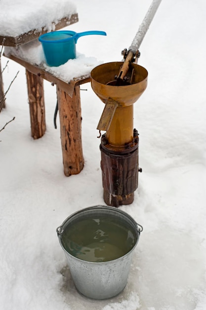 Balde de água potável limpa fica ao lado do poço e da bomba manual no pátio da vila