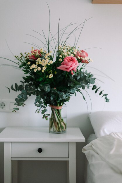 Foto balde de flores silvestres em uma base na mesa de cabeceira ao lado da cama branca. estilo nórdico.
