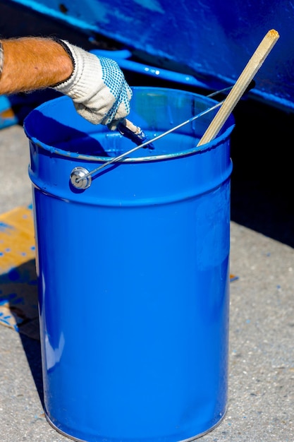 Balde de metal com tinta azul uma mão em uma luva protetora segura um pincel