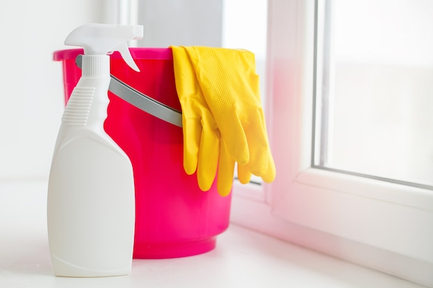 Un balde de plástico rosa y guantes amarillos sobre un alféizar blanco