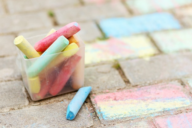 Un balde de tiza de colores sobre el asfalto en caja de plástico. Dibujar con tiza en el pavimento. crayones multicolores para dibujar.