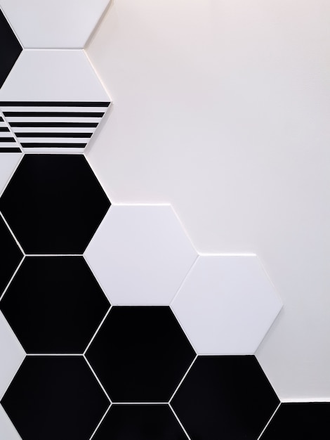 Una de baldosas de cerámica en blanco y negro en forma de hexágono que cubre parcialmente una pared blanca. Textura del concepto,