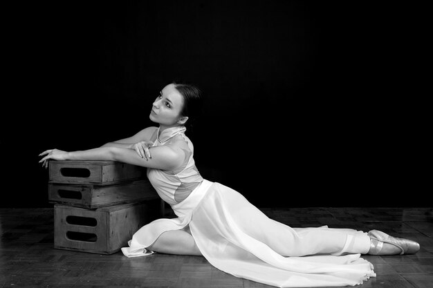 Foto balerina em um vestido branco e sapatos de ponta senta-se no chão em um fundo preto