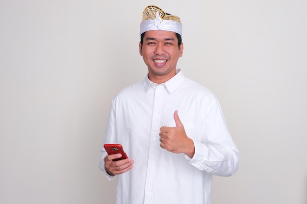 Balinesischer Mann lächelt und hebt den Daumen, während er ein Mobiltelefon hält