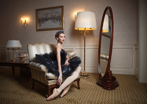 Foto ballerina im schwarzen tutu, das im sessel im luxusinnenraum sitzt