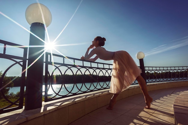 Ballerina in Chopin mit schönen Füßen geht barfuß an einem Sommertag am Terrassenzaun entlang