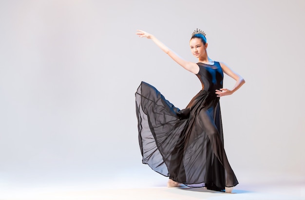 Ballerina in Spitzenschuhen und einem langen schwarzen Kleid, das in einer anmutigen Pose auf einer weißen Wand aufwirft