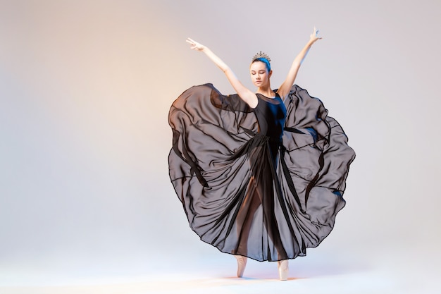 Ballerina in Spitzenschuhen und einem langen schwarzen transparenten Kleid, das auf einer weißen Wand tanzt