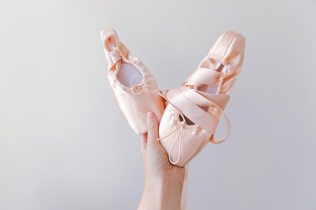 Ballerina-Tänzerin Hand hält neue pastellbeige Ballettschuhe mit Satinband isoliert auf weißem Rücken