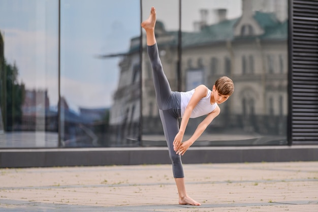 Ballettjunge Teenager trainiert auf seinen Händen vor dem Hintergrund der Reflexion der Stadt und des Himmels in der Glaswand