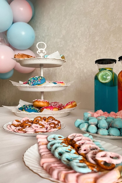 Balões azuis e rosa de festa de gênero no fundo de uma mesa festiva com donuts de limonadas de bolo e pretzels