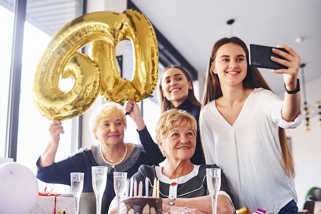 Balões com número 60. Mulher sênior com família e amigos, comemorando um aniversário dentro de casa.