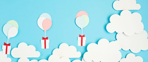 Balões cortados em papel e caixa de presente flutuando no céu azul com nuvens