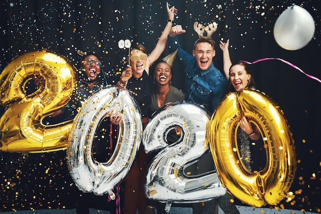 Balões de ano novo e amigos com confete em 2020 animados para a celebração do festival de festas e futuro glamour do evento social e retrato de grupo de homens e mulheres no estúdio para contagem regressiva festiva