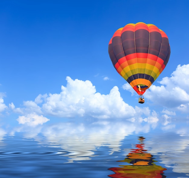 Balões de ar quente coloridos em voo sobre o céu azul com reflexo de água