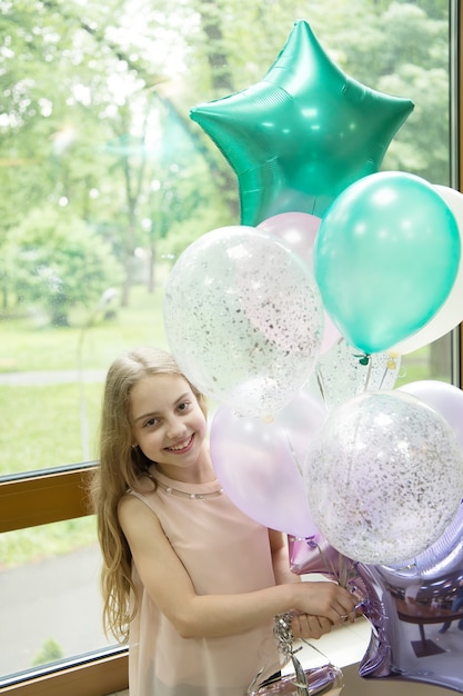 Balões e músicas de aniversário. Feliz menina bonitinha comemorando o feriado com balões de festa. Adorável criança pequena sorrindo com um monte de balões de ar. O hélio faz seus balões crescerem para a ocasião.