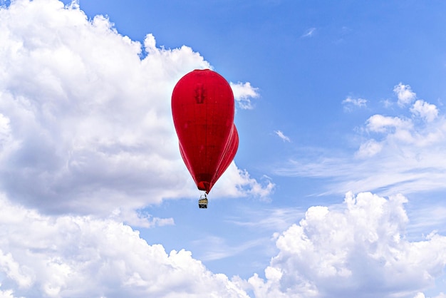 Balón de aire caliente en forma de corazón rojo volando sobre un cielo azul con nubes blancas