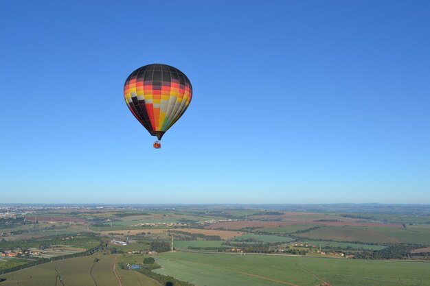 Foto balón de aire caliente volando sobre el paisaje contra un cielo azul claro