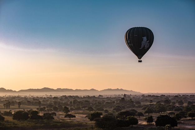 Balón de aire caliente volando sobre el paisaje contra el cielo durante la puesta de sol