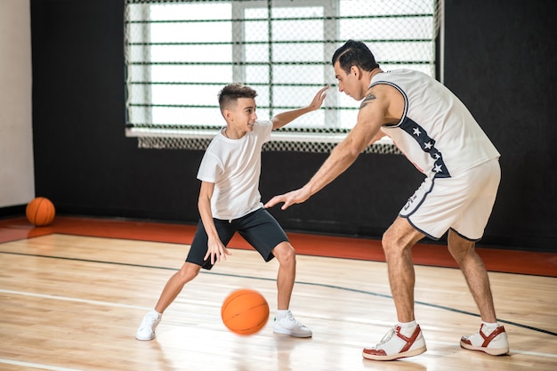 Baloncesto. Hombre moreno entrenando a una adolescente en el gimnasio