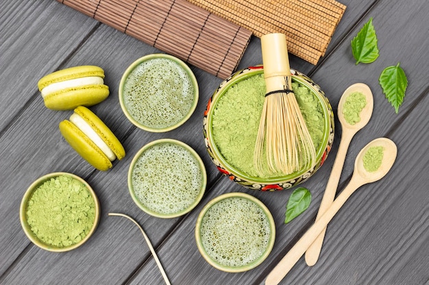 Bambusbesen in Schüssel mit Matcha-Pulver, Matcha-Grüntee-Makkaroni-Kuchen und Holzlöffel auf dem Tisch