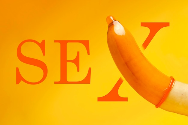 Foto banana de conceito de sexo seguro com preservativo em fundo amarelo