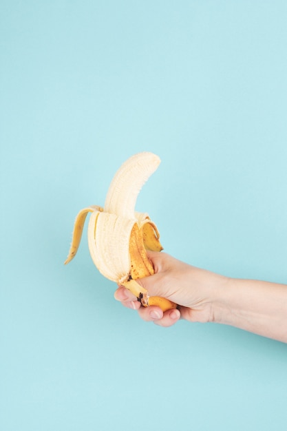 Banana madura descascada está em uma mão feminina em um fundo azul