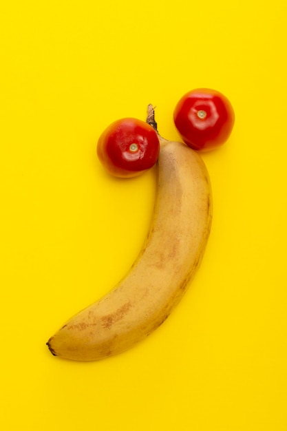 Banana madura e dois tomates vermelhos em um fundo amarelo