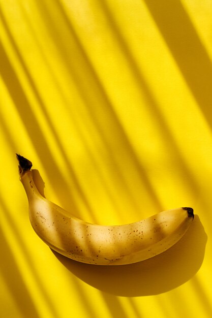 Foto banana orgânica doce madura crua uma no amarelo com sombras tropicais.