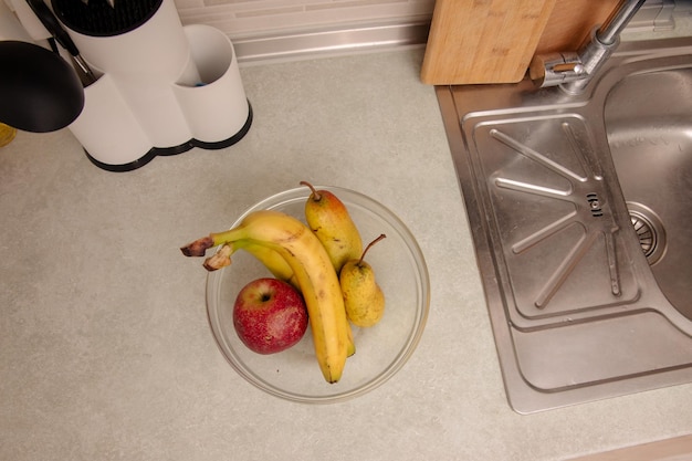 Bananas e maçãs em uma tigela de vidro na cozinha