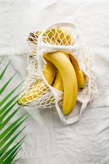 Bananas em um saco de produtos líquidos em um guardanapo de linho decorado com folha de palmeira Eco amigável e conceito de verão